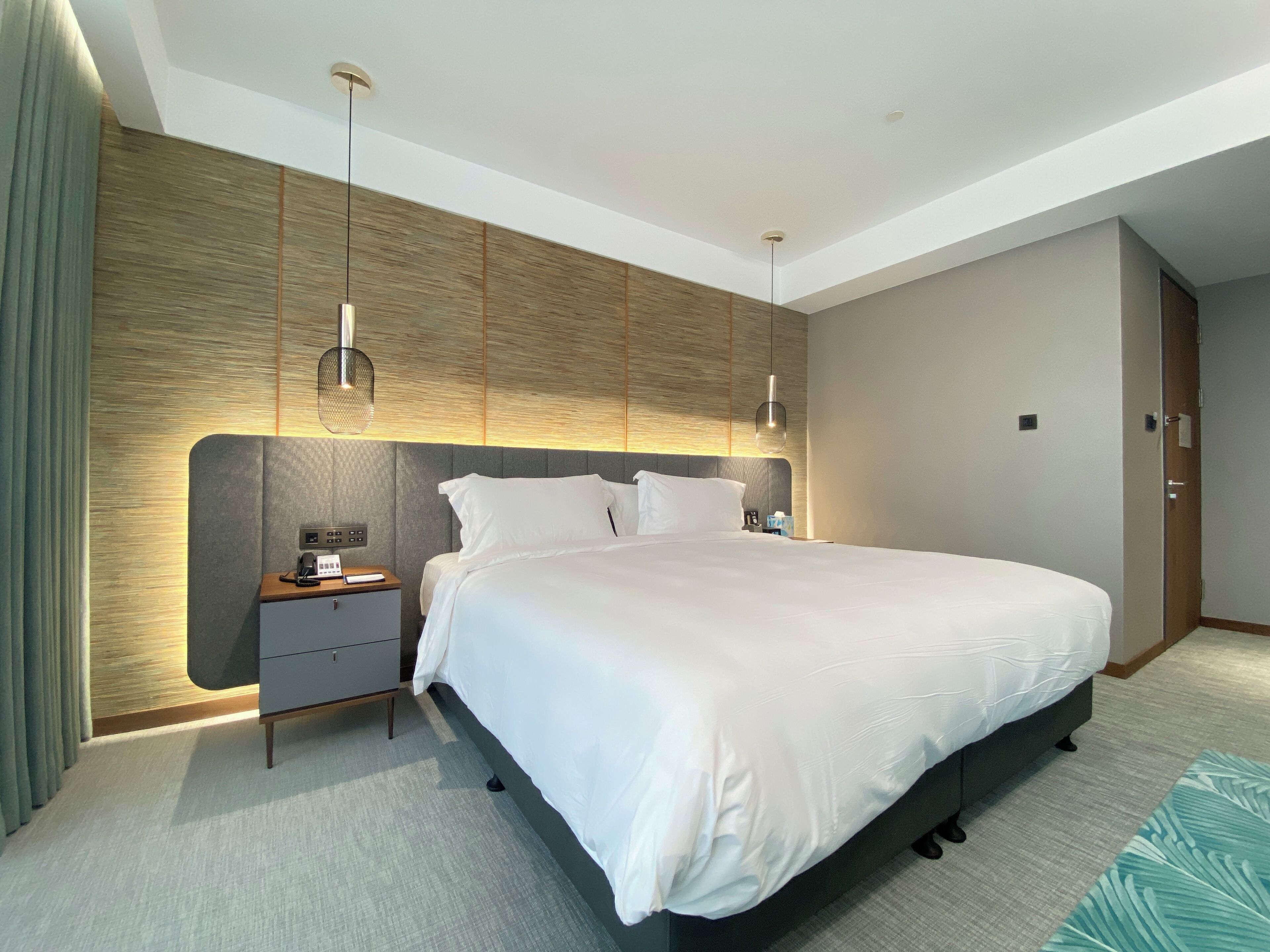 Una habitación de hotel moderna con una cama grande, mesitas de noche y una lámpara fijada a la pared.