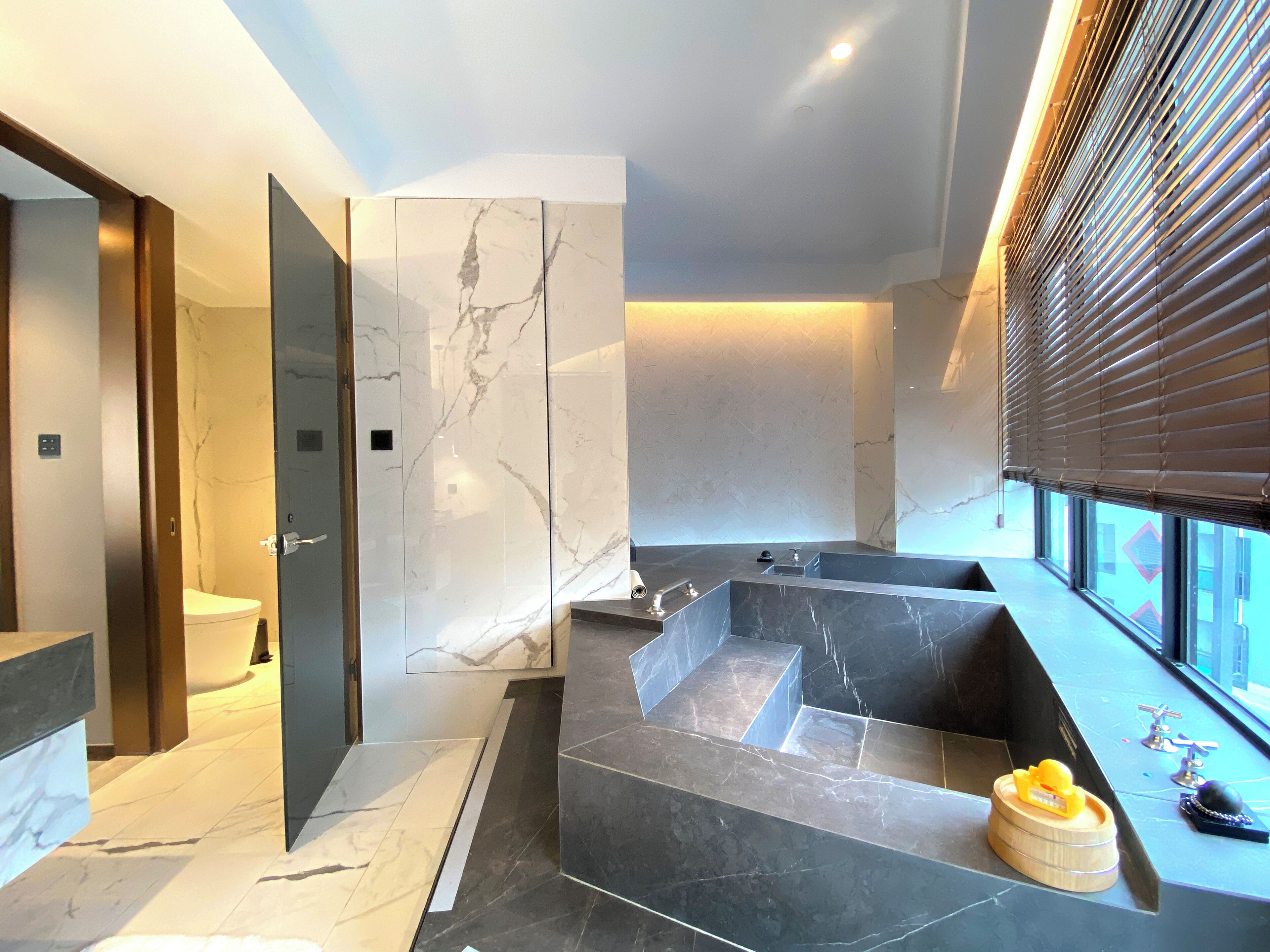 A modern bathroom with a marble vanity, a bathtub, and a toilet.