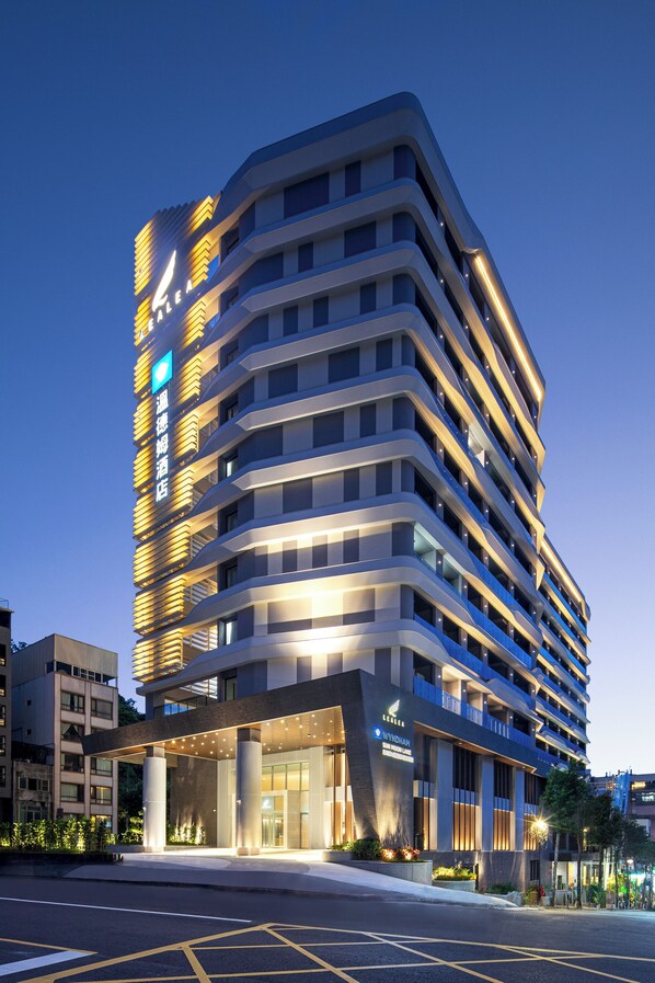 Un hotel moderno con fachada curva, varios balcones y una entrada bien iluminada.