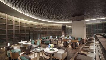 A modern lounge area with a curved ceiling, seating arrangements, and a large bookshelf in the background.
