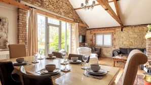 A dining area with a table set for four, a stone wall, and a high ceiling with exposed beams.