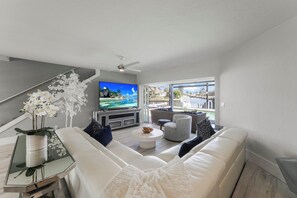 Un salon moderne avec un canapé blanc, une table basse, un téléviseur et un balcon offrant une vue dégagée.