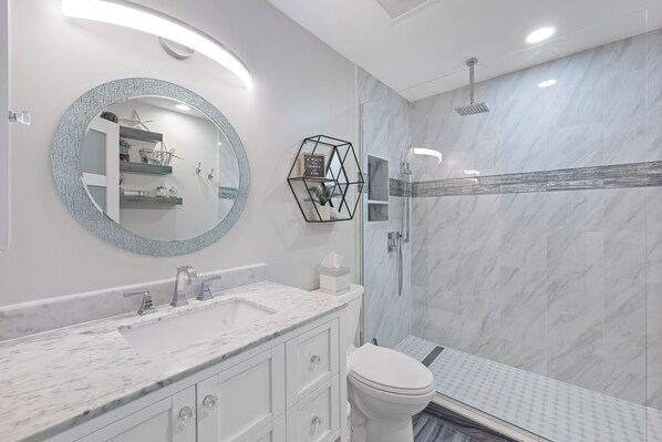 A modern bathroom with a marble vanity, a round mirror, a shower enclosure, and a toilet.