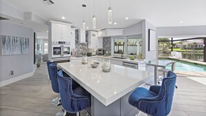 Una cocina moderna con una isla grande, taburetes de bar y vistas a una piscina.