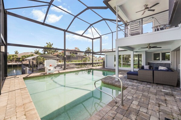 Une piscine entourée de parois en verre, un espace patio aménagé avec des sièges et une vue sur le quartier environnant.