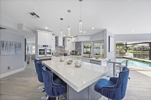 A modern kitchen with a central island, bar stools, and a view of a swimming pool.