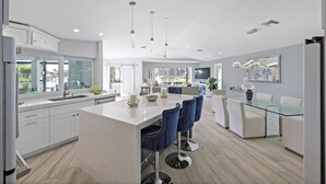 Una cocina moderna con armarios blancos, una isla central con taburetes y luminarias colgantes.