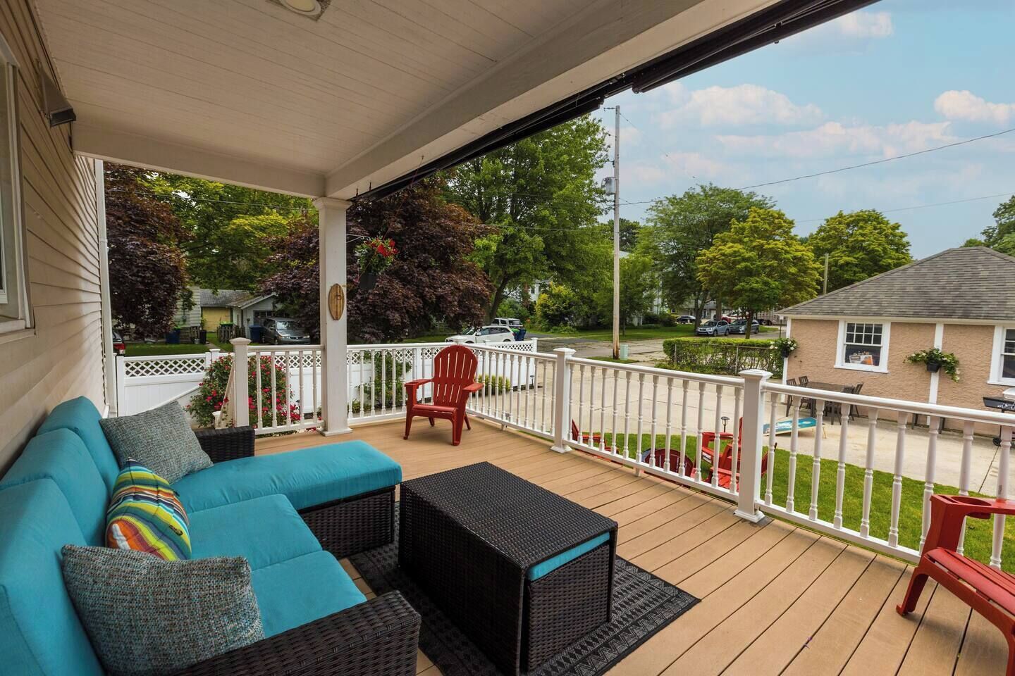 A covered porch with a blue sofa, a red chair, and a black wicker table.