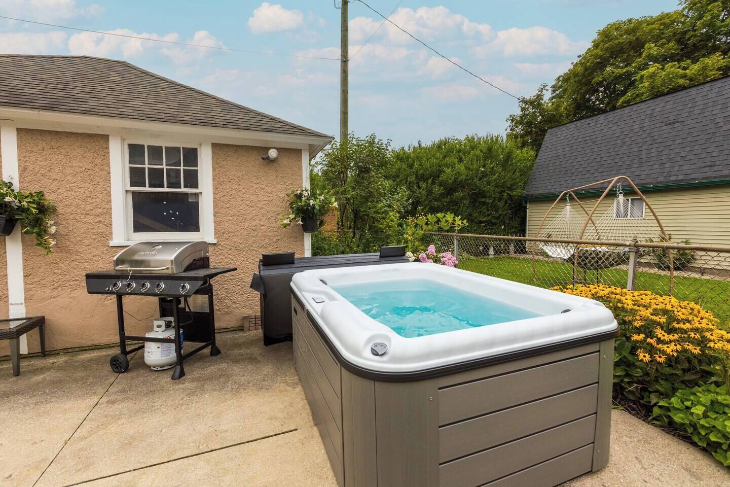 A backyard with a hot tub, a grill, and a small table.