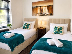 A hotel room with two beds, a painting above the beds, a nightstand with lamps, and a window with blinds.