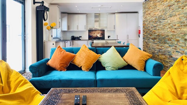 A modern living room with a blue sofa, colorful cushions, a coffee table, and a kitchen in the background.