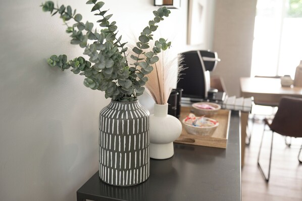 A modern kitchen with a dark countertop, a striped vase with green foliage, a white vase, and a wooden tray with food items.