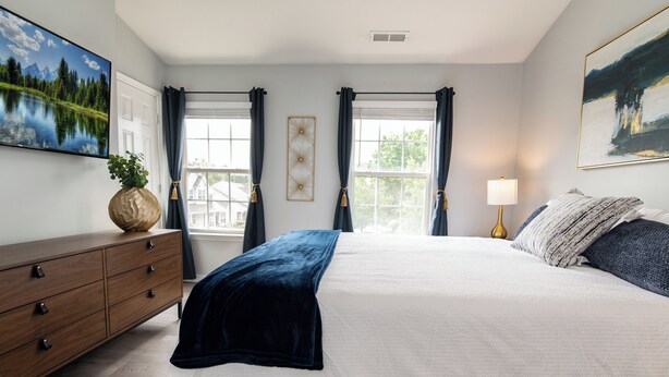 Une chambre à coucher avec un grand lit, une commode, une lampe et un tableau au mur.