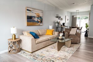 Ein Wohnzimmer mit einem beigefarbenen Sofa, einem Glastisch und einem gemusterten Teppich.