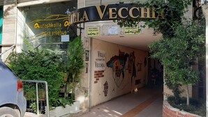 The entrance to Villa Vecchia, a restaurant with a mural on the wall, and a sign indicating parking availability. - Room-enki's Guesthouse Tirana (Tirana)
