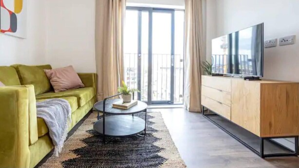 A modern living room with a green sofa, a round coffee table, and a TV on a wooden cabinet. - Exquisite 1-bed Homely Apartment in Manchester (Salford)