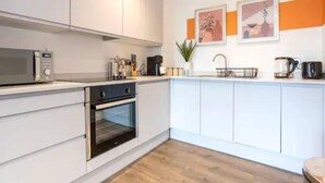 A modern kitchen with white cabinets, a built-in oven, a microwave, and a coffee maker. - Exquisite 1-bed Homely Apartment in Manchester (Salford)