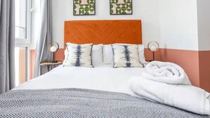 A neatly made bed with a patterned bedspread, two pillows with a tree design, and a folded white towel on the side. - Exquisite 1-bed Homely Apartment in Manchester (Salford)
