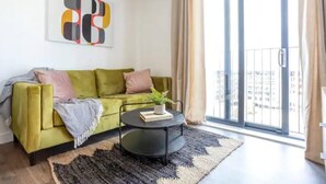 A modern living room with a green sofa, a round black coffee table, and a large window with curtains. - Exquisite 1-bed Homely Apartment in Manchester (Salford)