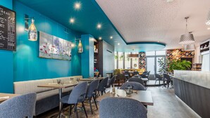 A modern restaurant interior with teal walls, wooden flooring, and a mix of grey and black upholstered seating. - Hôtel Restaurant Le Victoria (Rennes)