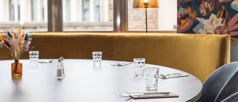 Una mesa redonda con sillas, un jarrón con flores secas y una planta colgante.
