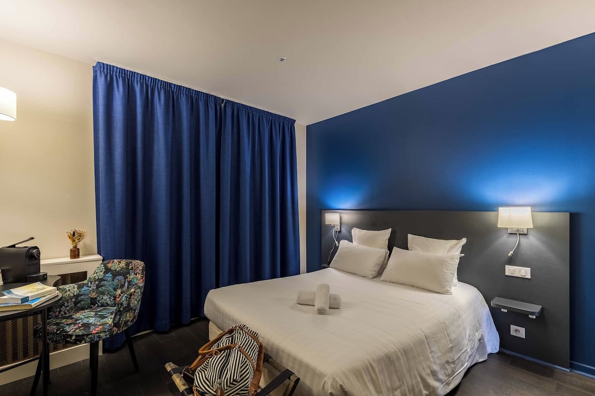 A hotel room with a bed, a desk, a chair, and a window with blue curtains.