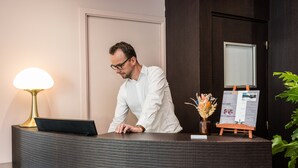 A reception desk with a lamp, a small stand with a sign, and a potted plant. - Hôtel Restaurant Le Victoria (Rennes)