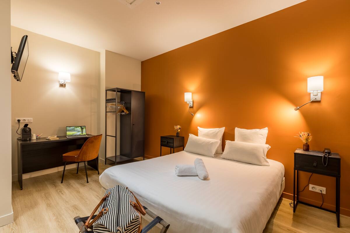 A hotel room with a bed, a desk, a chair, a wardrobe, and bedside tables with lamps.