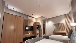 A hotel room with two beds, a TV, a wardrobe, and an air conditioning unit. - السعاده سويت للشقق المخدومه (Riyadh)