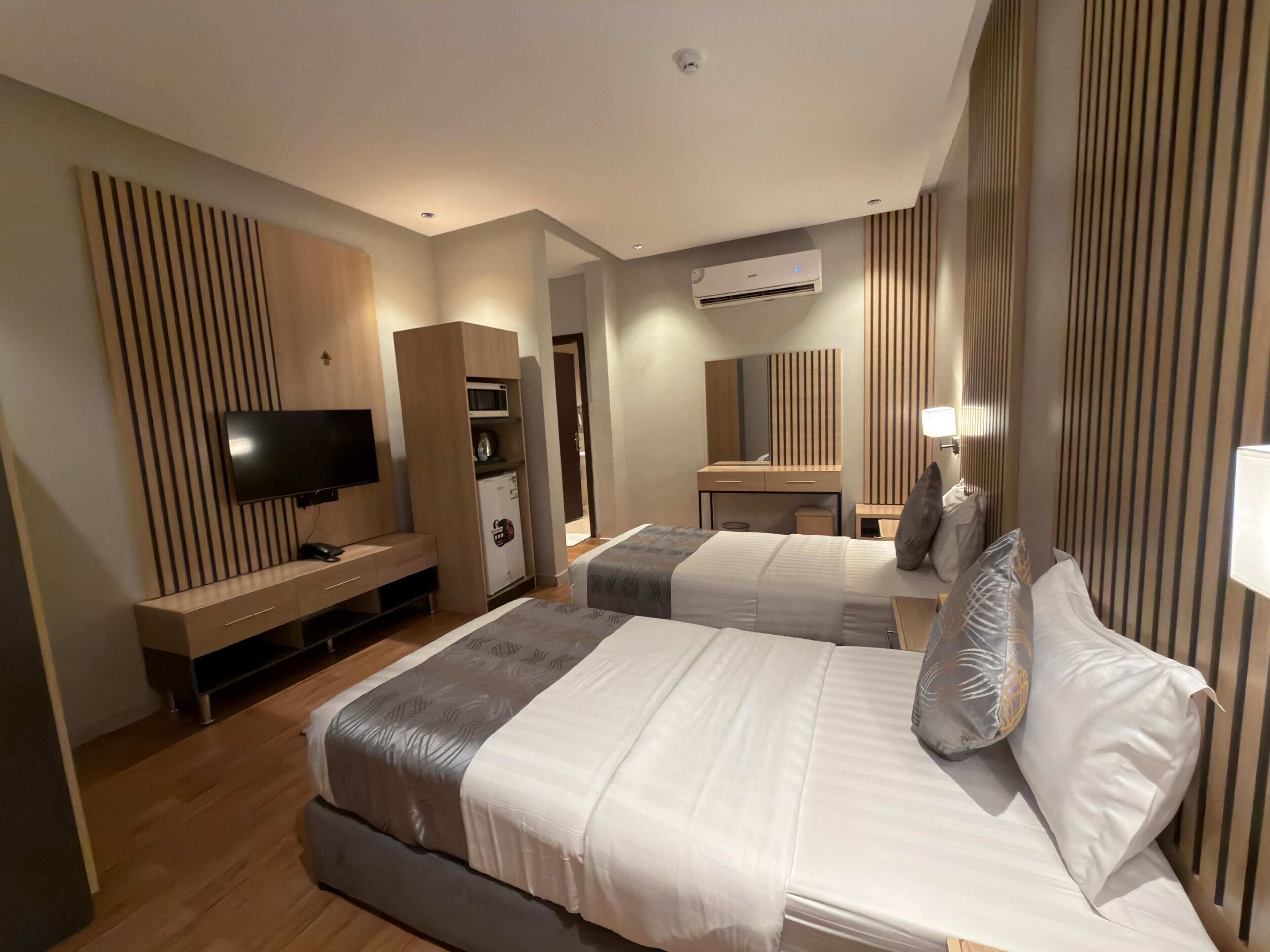 Habitación de hotel con dos camas, televisión, minibar y espejo.