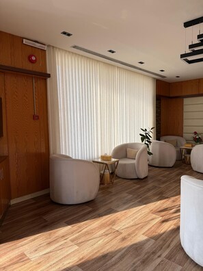 Un salon moderne avec un plancher en bois, une grande fenêtre équipée de stores et un ensemble de canapés.