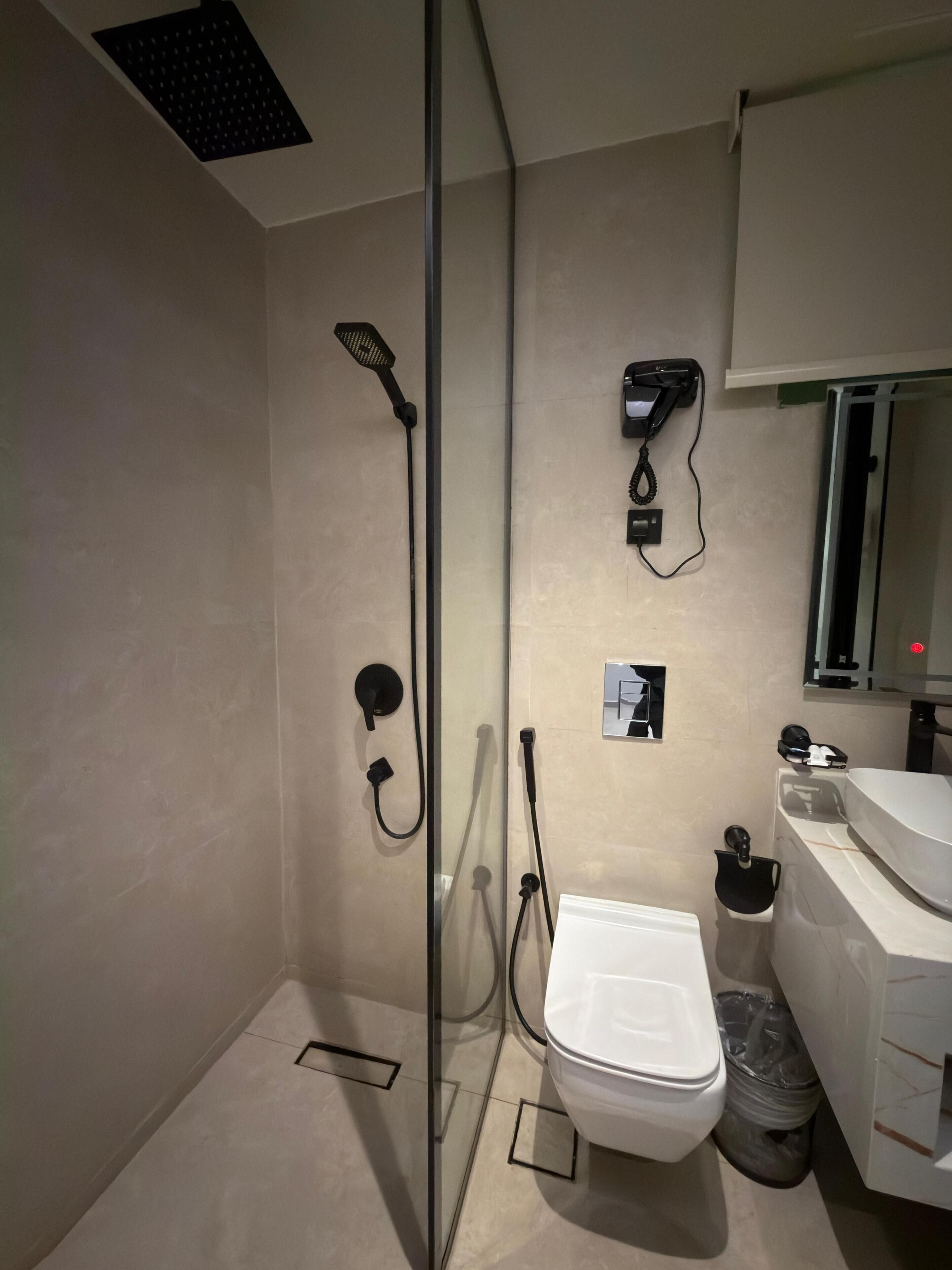 Een moderne badkamer met een glazen douchecabine, een toilet, een wastafel en een aan de muur bevestigde telefoon.