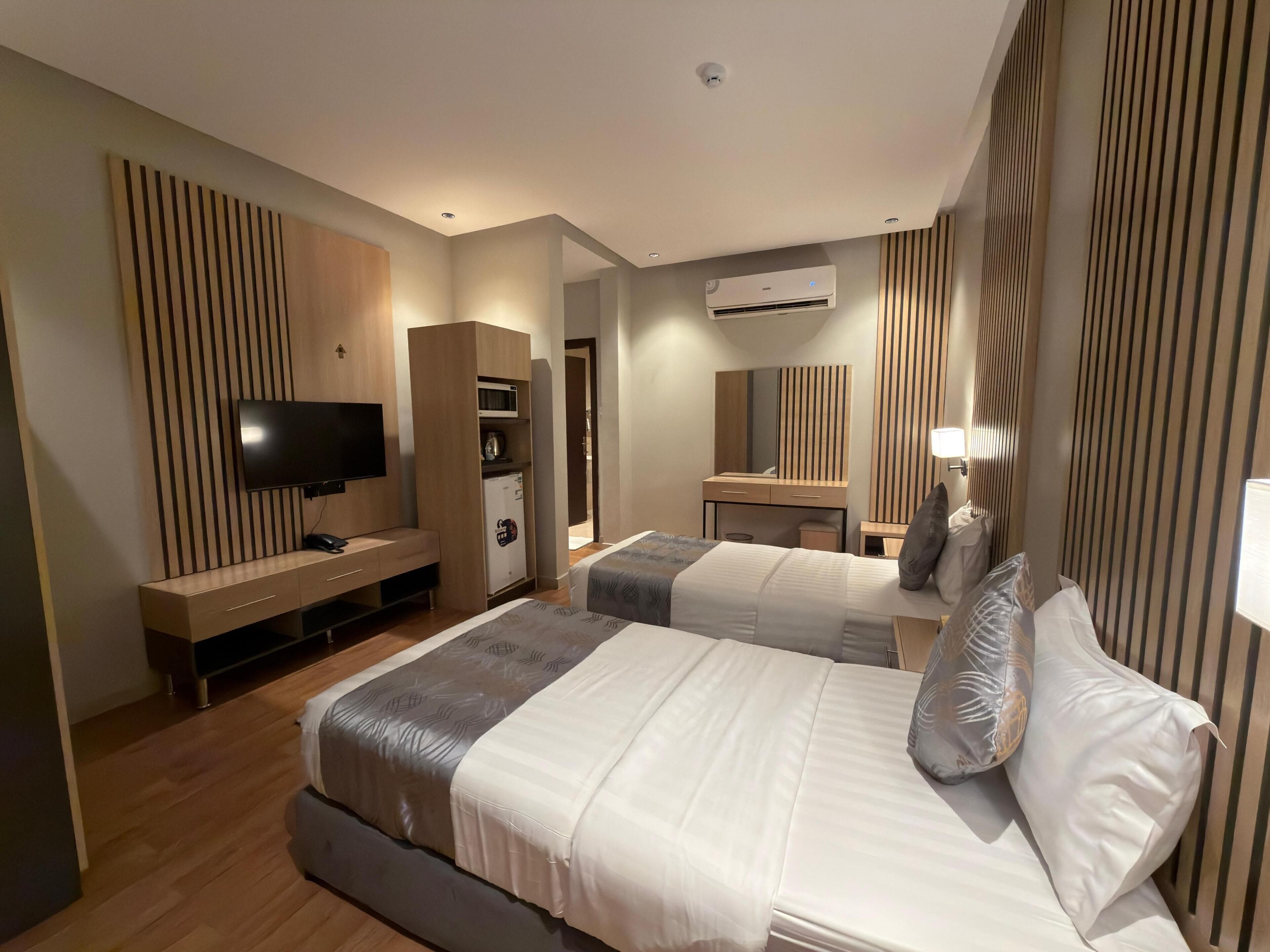 Ein Hotelzimmer mit zwei Betten, einem Fernseher, einer Minibar und einem Spiegel.