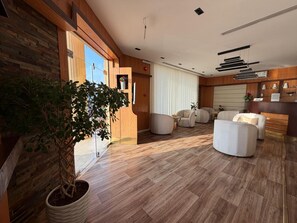 Ein modernes Interieur mit einer Holzvertäfelung, einer Topfpflanze und einer Sitzecke mit Sofa und Sesseln.