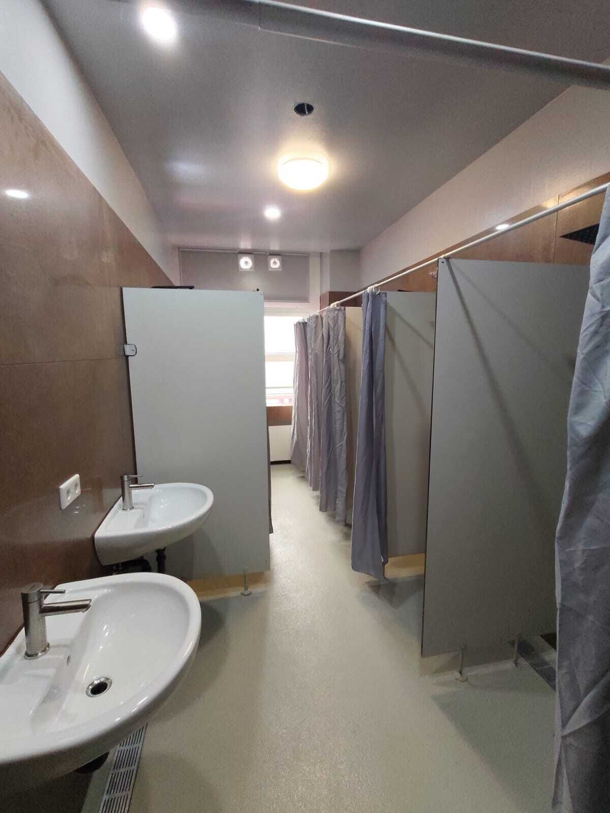Une salle de bain moderne avec une rangée de cabines individuelles, un lavabo et un miroir.
