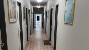 A long hallway with wooden flooring, doors on both sides, and framed pictures on the walls. - Sitya Hostel München (Munich)