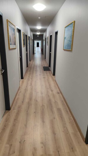 A long hallway with wooden flooring, doors on both sides, and framed pictures on the walls. - Sitya Hostel München (Munich)