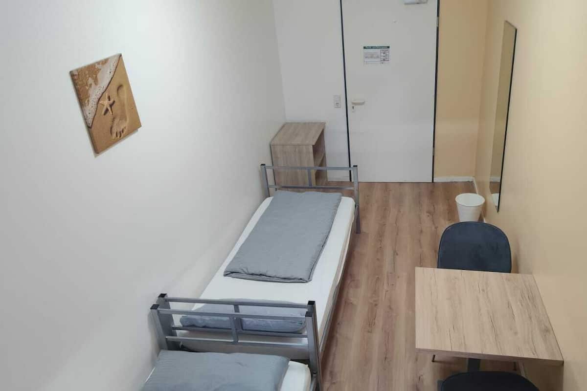 Een kleine, praktische kamer met een enkel bed, een houten bureau en een stoel.