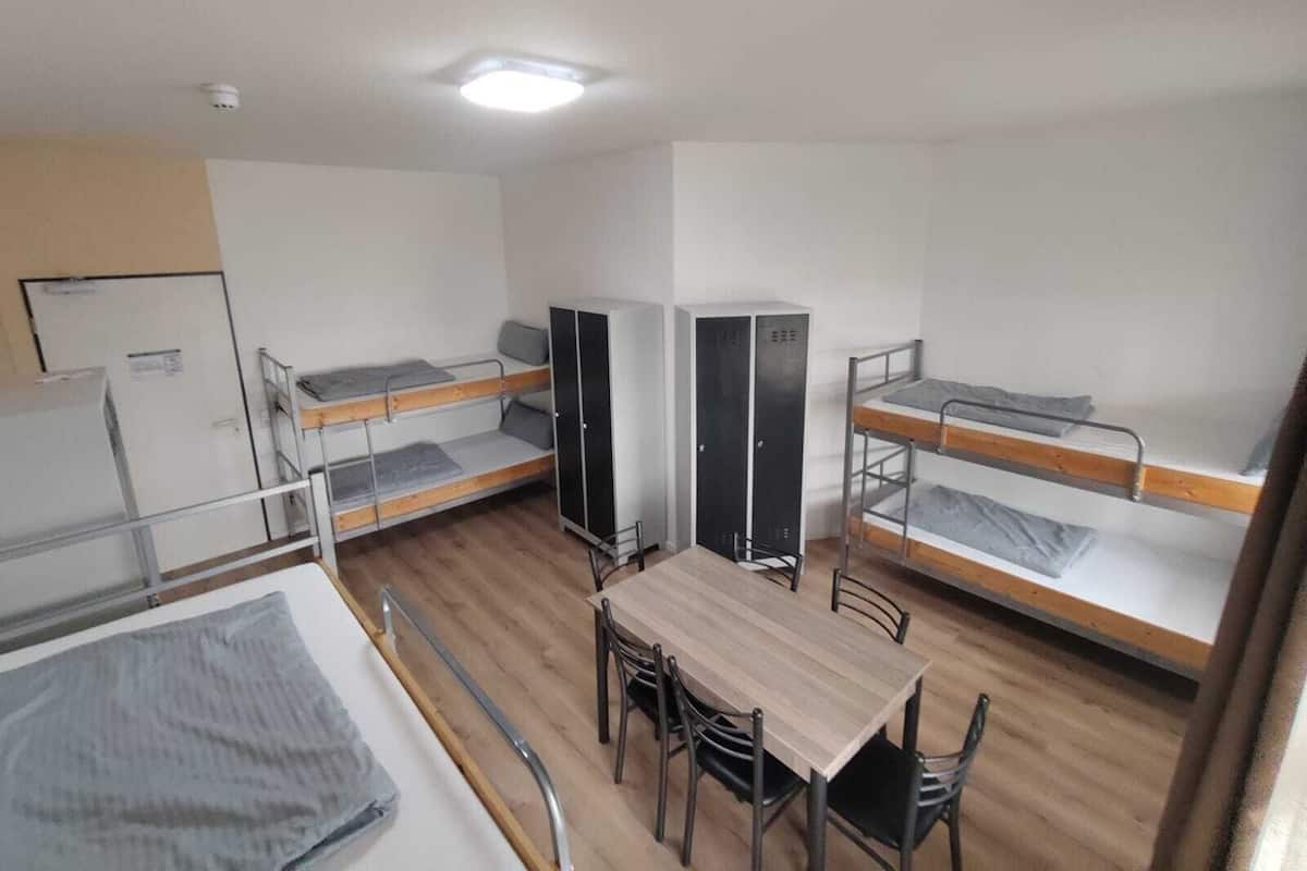 Een slaapzaal met stapelbedden, een tafel, stoelen, een kledingkast en een bureau.