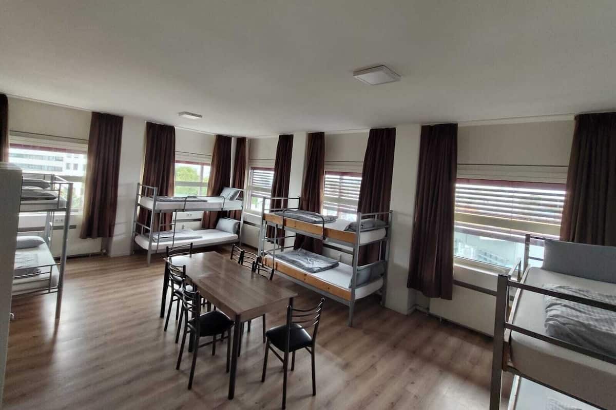 Een slaapzaal met stapelbedden, een houten tafel en stoelen.