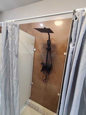 A shower with a rain showerhead and a handheld showerhead mounted on a wall. - Sitya Hostel München (Munich)