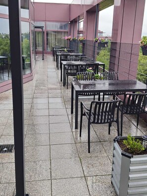 An outdoor patio area with multiple tables and chairs, a glass enclosure, and potted plants. - Sitya Hostel München (Munich)