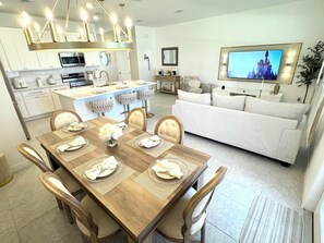 A modern kitchen with a dining area, a living room with a TV, and a sofa.