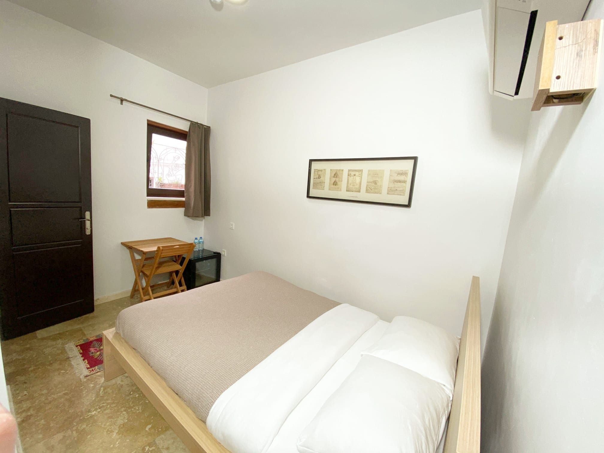 Una camera da letto con un letto, una scrivania, una sedia, una finestra con tende e un quadro appeso al muro.