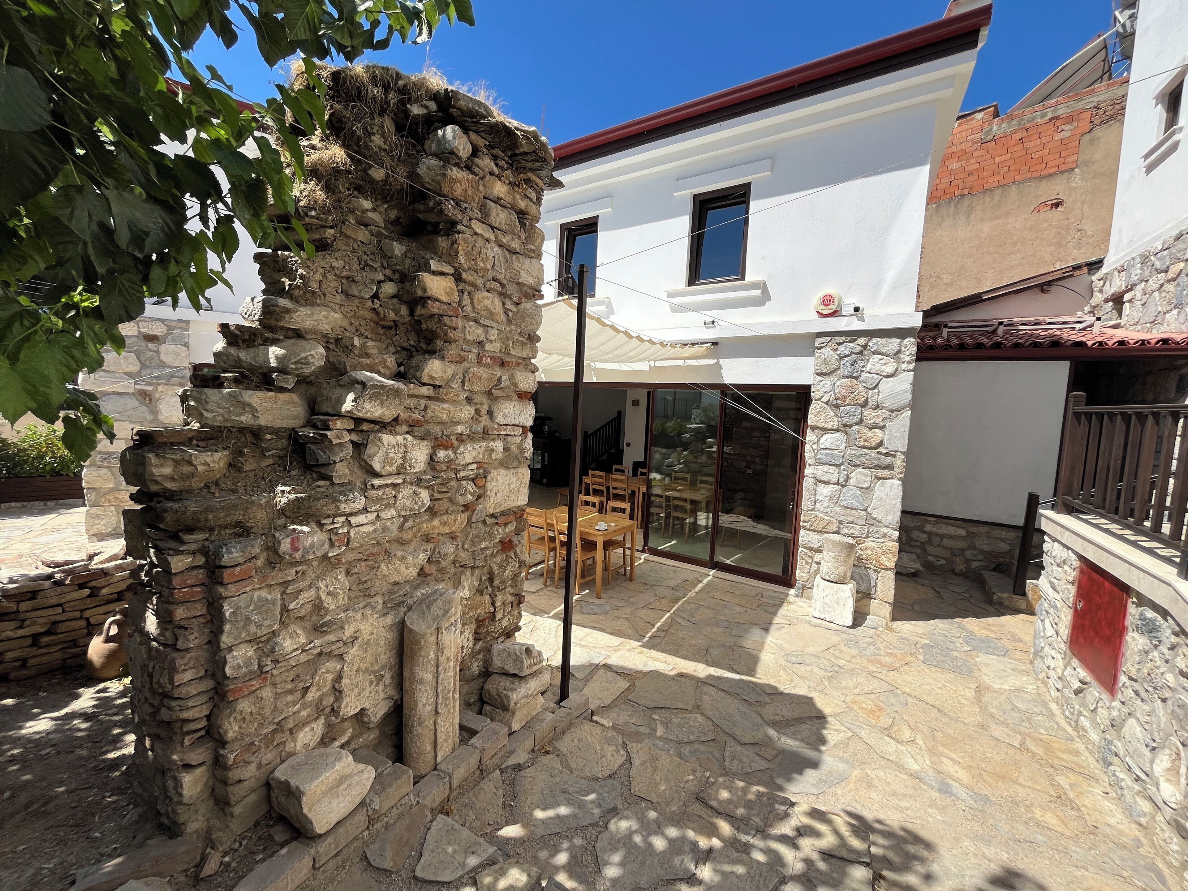 A stone structure with a patio area, a white building with a red roof, and a glass door leading to an interior space.