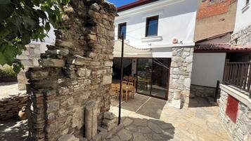 A stone structure with a patio area, a white building with a red roof, and a glass door leading to an interior space.