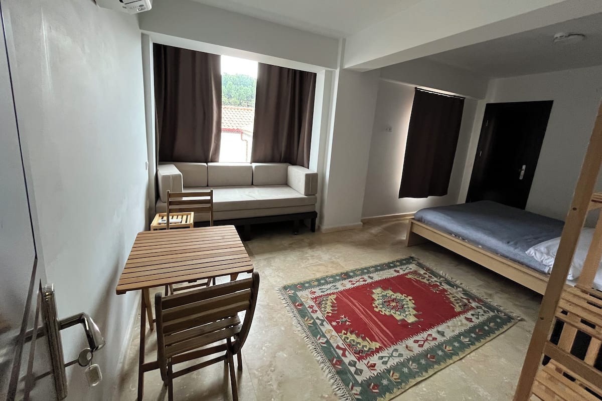 A compact room with a sofa, a small table, a bed, and a window with curtains.