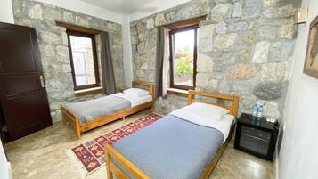 A room with two wooden beds, a ceiling fan, stone walls, and a small table with water bottles.