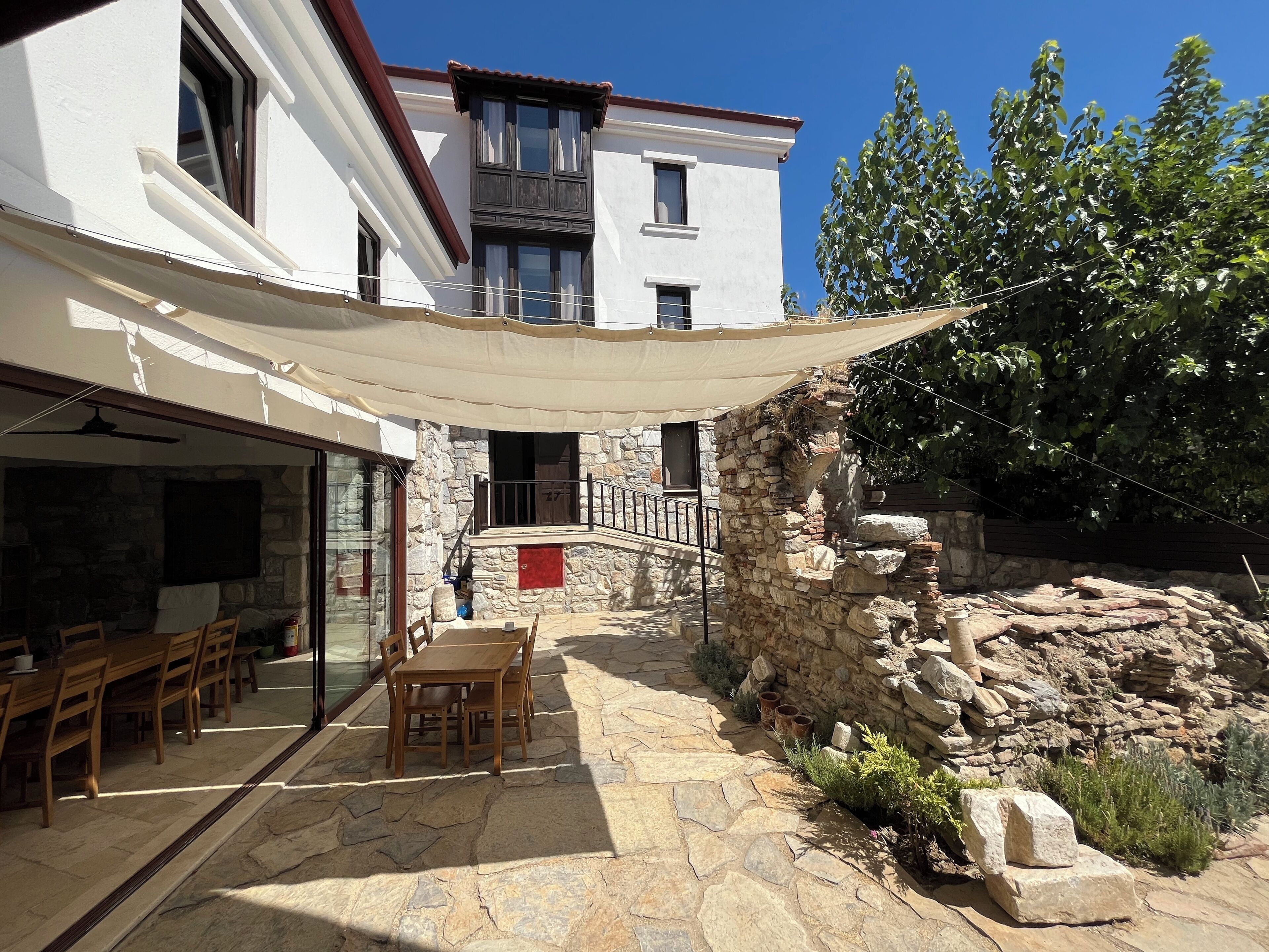 A stone patio with outdoor seating, a stone wall, and a white building with windows and a balcony.