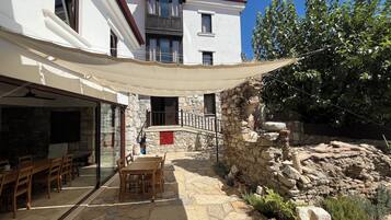 A stone patio with outdoor seating, a stone wall, and a white building with windows and a balcony.